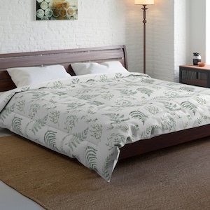 May include: A bedroom scene featuring a dark wood bed frame with a white and green botanical print comforter. The room has a neutral color palette with a brown rug, white walls, and a floor lamp. A piece of abstract art hangs on the wall.