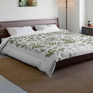 May include: A white duvet cover with a green botanical print featuring various leaves and ferns. The duvet cover is on a bed with a wooden headboard and a brown rug.