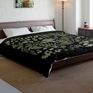 May include: A black duvet cover with a green and white botanical print featuring leaves and flowers. The duvet cover is on a bed with white pillows and a brown wooden headboard.