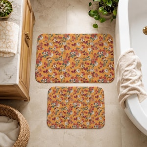 May include: Two rectangular bath mats featuring a mustard yellow background with a dense, repeating pattern of small flowers in shades of red, white, pink, and teal green. The mats have rounded corners and a soft, flat-weave textile surface.