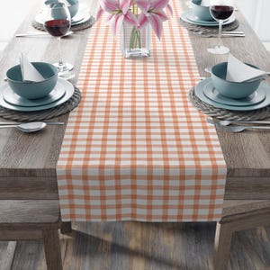May include: A peach and white checkered table runner. The runner is laid out on a wooden table with place settings on either side.
