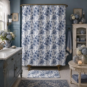May include: A white shower curtain and matching rectangular bath mat featuring a repeating dark blue floral toile pattern. The shower curtain hangs from a brass rod with rings, and the bath mat is positioned on the floor in front of the tub.