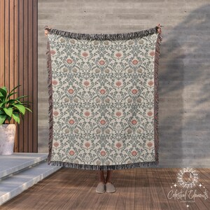May include: A woven tapestry throw blanket with a floral pattern in shades of pink, green, and cream. The blanket has a fringe border.