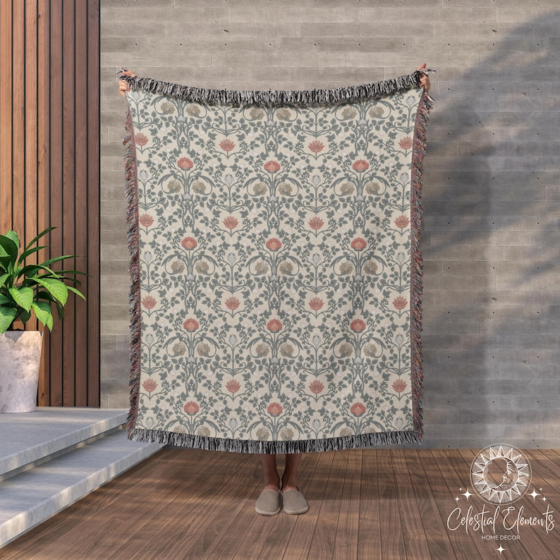 May include: A woven tapestry throw blanket with a floral pattern in shades of pink, green, and cream. The blanket has a fringe border.