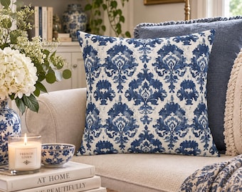 May include: A square throw pillow featuring a blue and white damask pattern. The fabric displays a repeating ornate floral motif in deep blue ink tones against a crisp white background, creating a high-contrast visual effect on the cushion.
