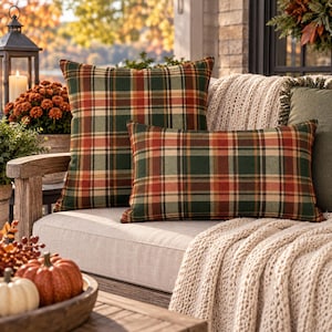 May include: Two decorative throw pillows featuring a plaid pattern in shades of forest green, burnt orange, and cream. One pillow is square and the other is rectangular, both made of fabric with a visible weave, displayed on a light-colored sofa.