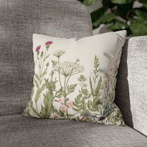 May include: A white throw pillow with a floral pattern featuring various green leaves, pink, white, and blue flowers.