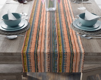 May include: A colorful table runner with a geometric pattern in shades of blue, green, orange, and brown. The runner is laid on a wooden table with place settings on either side.