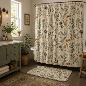 May include: A shower curtain and matching bath mat featuring a botanical print with various wildflowers, grasses, and foliage in muted tones of orange, purple, and green against a cream-colored background, suspended from a dark metal rod.