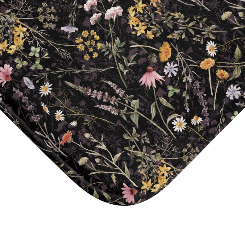 K&ouml;nnte beinhalten: Eine schwarze Badematte mit einem Blumenmuster, das verschiedene Blumen in den Farben Rosa, Gelb und Lila zeigt. Die Blumen sind in einem zuf&auml;lligen Muster auf einem dunklen Hintergrund angeordnet.
