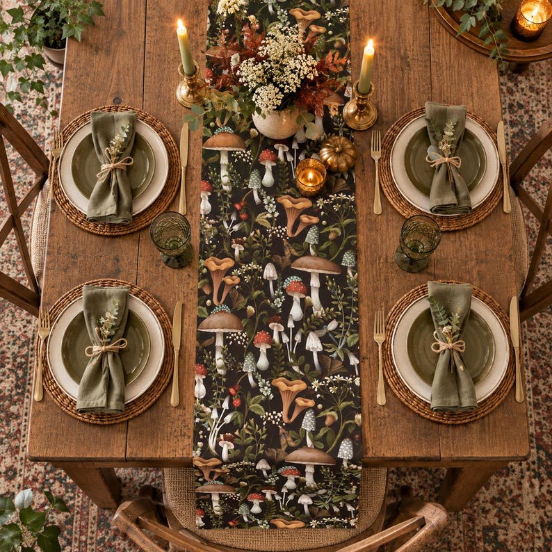 May include: A wooden dining table set for four with a black table runner featuring a colorful mushroom and botanical print. Each place setting includes a woven placemat, a white plate, a green plate, a green napkin, and a gold-toned flatware set.