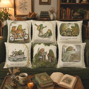 May include: A set of six square throw pillows featuring illustrations of two frogs in various scenes. The designs include frogs on a tandem bicycle, sitting in a boat, eating, reading in bed, and interacting with text captions from the Frog and Toad series.
