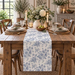 May include: A rectangular table runner featuring a blue and white floral pattern draped down the center of a wooden dining table. The runner displays intricate botanical illustrations of various flowers and leaves across its entire surface.