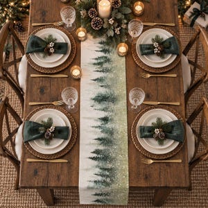 May include: A rectangular table runner featuring a watercolor-style forest of green pine trees on a light background, centered on a wooden dining table set with four place settings, each including woven placemats, white plates, and dark green napkins.