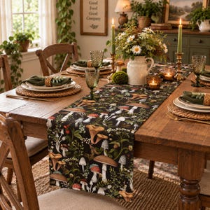 May include: A dark-colored table runner featuring a detailed botanical print of various mushrooms, ferns, and small white flowers. The runner is laid across a wooden dining table set with woven placemats, green napkins, and glassware.