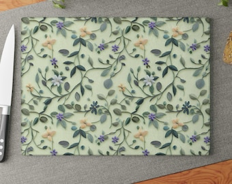 May include: A green glass cutting board with a floral pattern featuring white, yellow, and purple flowers and green leaves.