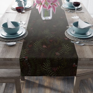 May include: A dark green table runner with a floral pattern featuring ferns, leaves, and butterflies. The runner is laid out on a wooden table with place settings on either side.