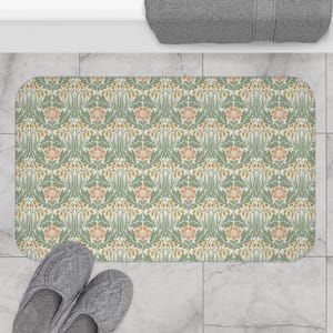 May include: Rectangular bath mat with a repeating floral pattern in shades of green, peach, and gold. The mat has rounded corners and is placed on a tiled floor. A pair of gray slippers are at the bottom.