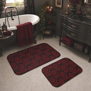 May include: A set of two rectangular bathroom rugs featuring a black background with a repeating deep red damask pattern. The rugs have rounded corners and a dark trim along the edges, providing a consistent look for a bathroom floor space.