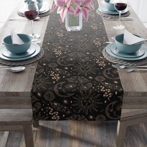 May include: Black table runner with a gold celestial pattern featuring moons, suns, stars, and snakes. The pattern is repeated throughout the runner.