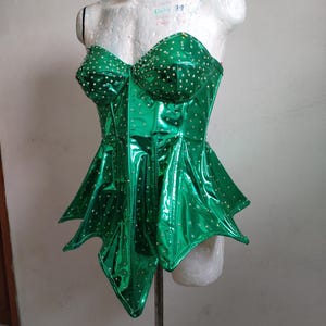 May include: A green, shiny, strapless corset with a pointed, layered skirt. The corset is covered in small, silver rhinestones.