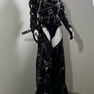 May include: A black leather outfit with a studded design. The outfit includes a corset with a silver chain and a pair of chaps with a silver buckle.