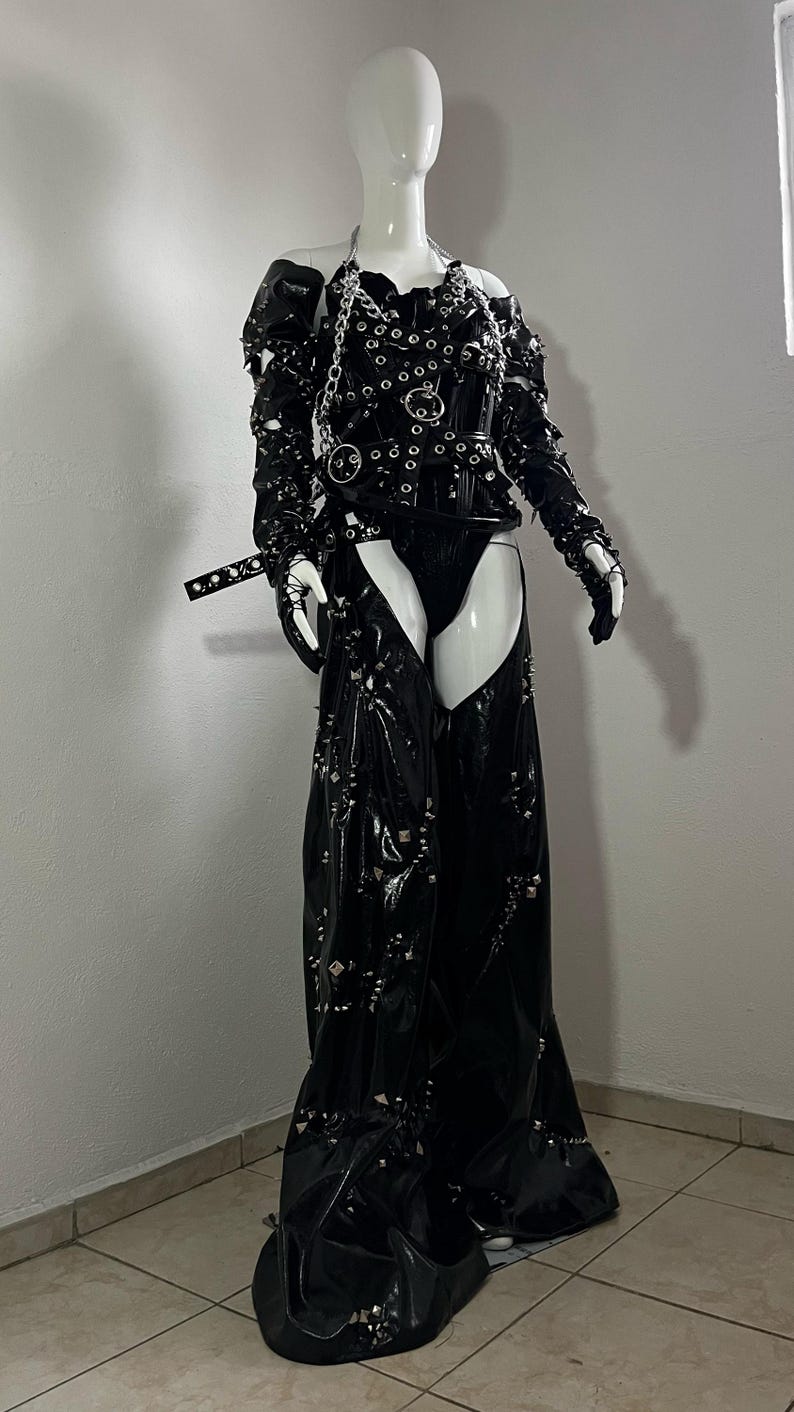 May include: A black leather outfit with a studded design. The outfit includes a corset with a silver chain and a pair of chaps with a silver buckle.