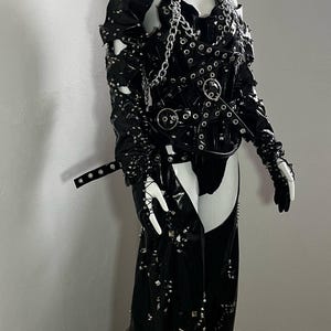 May include: A black leather outfit with silver studs and chains. The outfit includes a corset, trousers, and gloves.