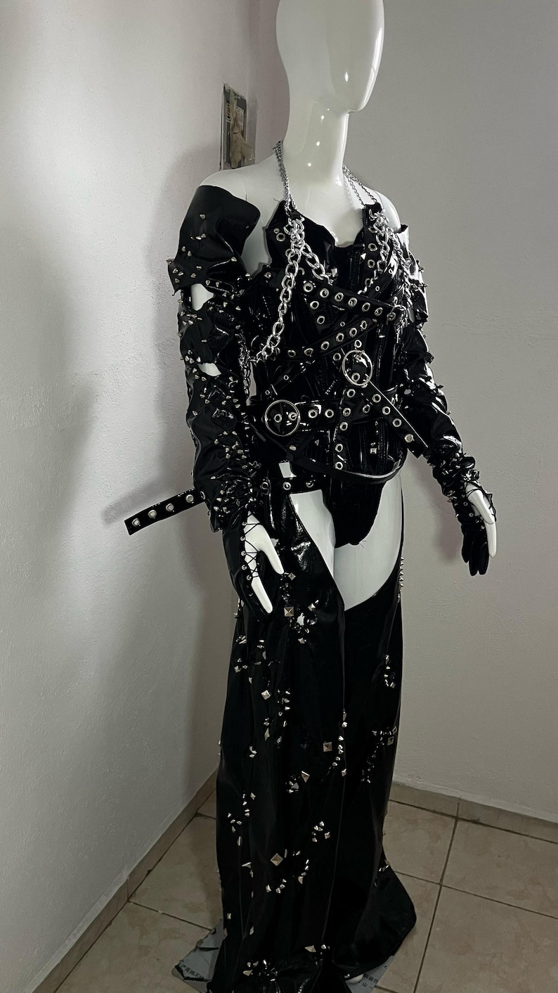 May include: A black leather outfit with silver studs and chains. The outfit includes a corset, trousers, and gloves.