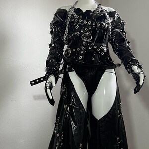 May include: A black leather outfit with silver studs and buckles. The outfit includes a corset, trousers, and gloves.