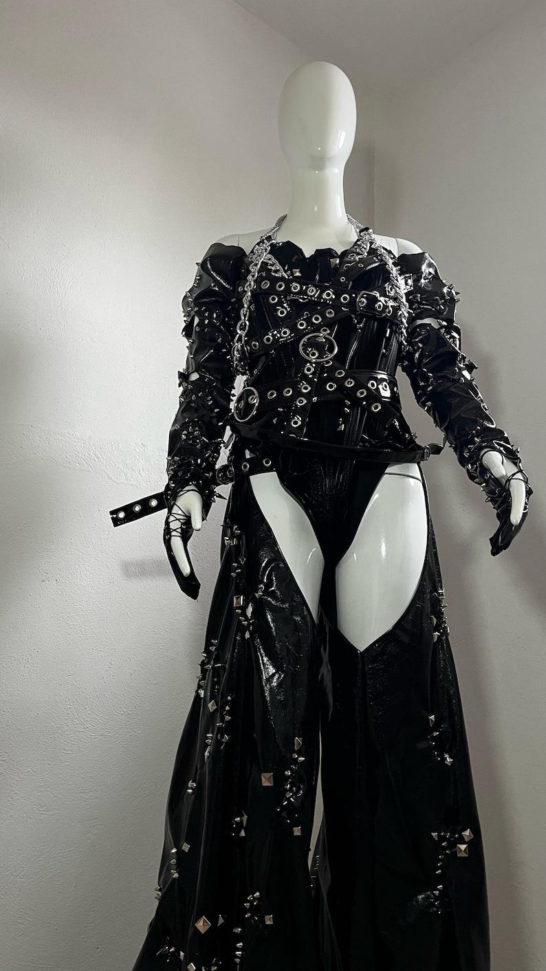 May include: A black leather outfit with silver studs and buckles. The outfit includes a corset, trousers, and gloves.