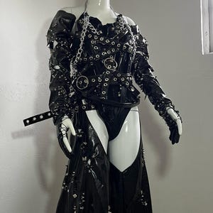 May include: A black leather outfit with silver hardware and studs. The outfit includes a corset with straps and a skirt with a high slit.