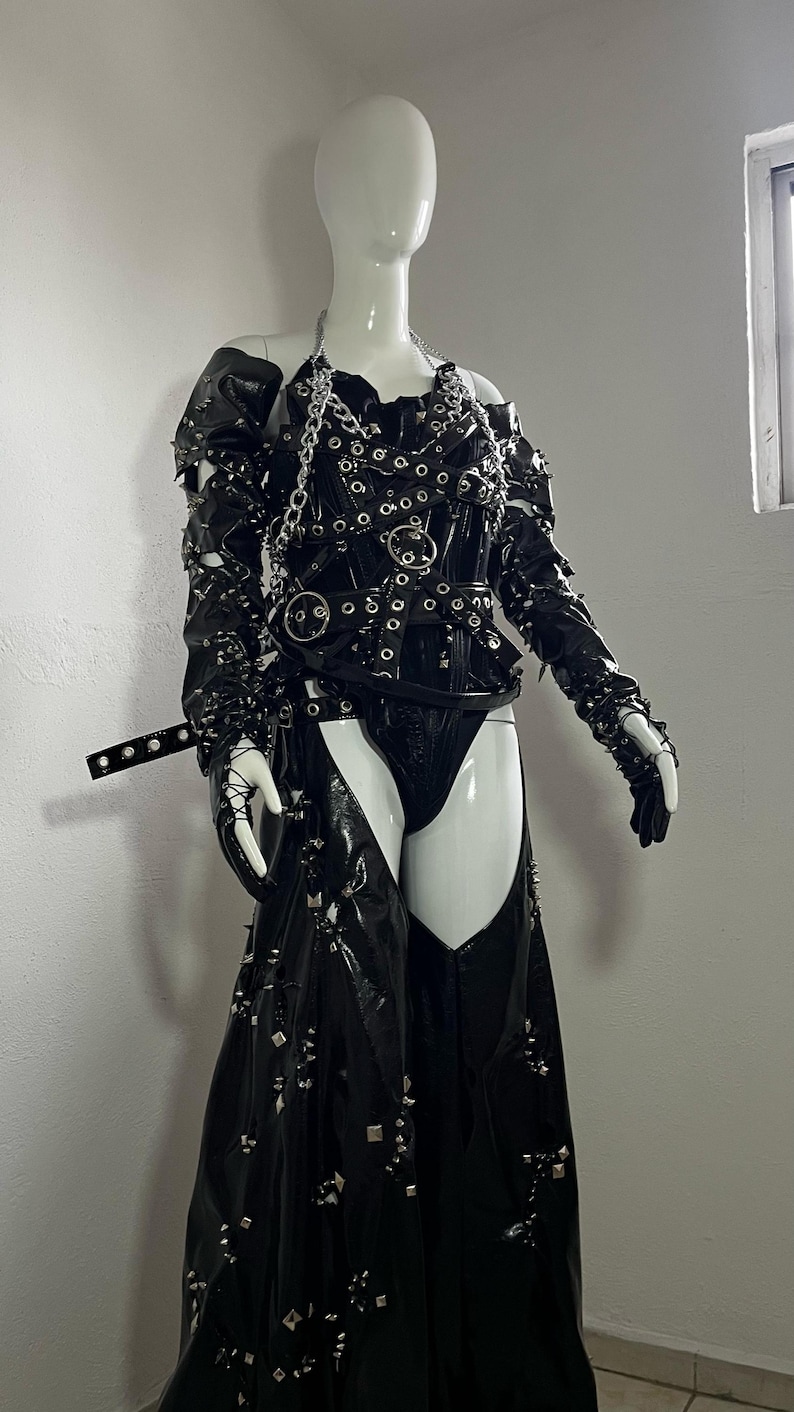 May include: A black leather outfit with silver hardware and studs. The outfit includes a corset with straps and a skirt with a high slit.