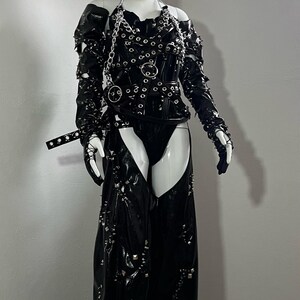 May include: A black leather outfit with silver hardware, including a corset, chaps, and gloves. The outfit is studded with silver accents and has a chain detail.