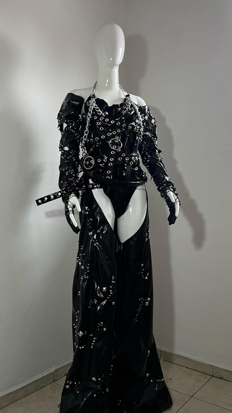 May include: A black leather outfit with silver hardware, including a corset, chaps, and gloves. The outfit is studded with silver accents and has a chain detail.