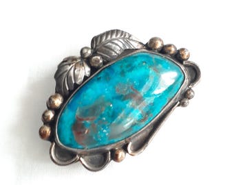 May include: A turquoise stone set in a silver ring with a leaf design. The ring is accented with small gold beads.