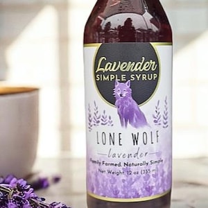 K&ouml;nnte beinhalten: Eine Glasflasche mit Lavendel-Sirup mit einer Illustration eines lila Wolfes auf dem Etikett. Das Etikett lautet "Lavender Simple Syrup" und "Lone Wolf - Lavendel - Familiengef&uuml;hrt. Nat&uuml;rlich einfach. Nettogewicht, 12 oz (355 ml)".