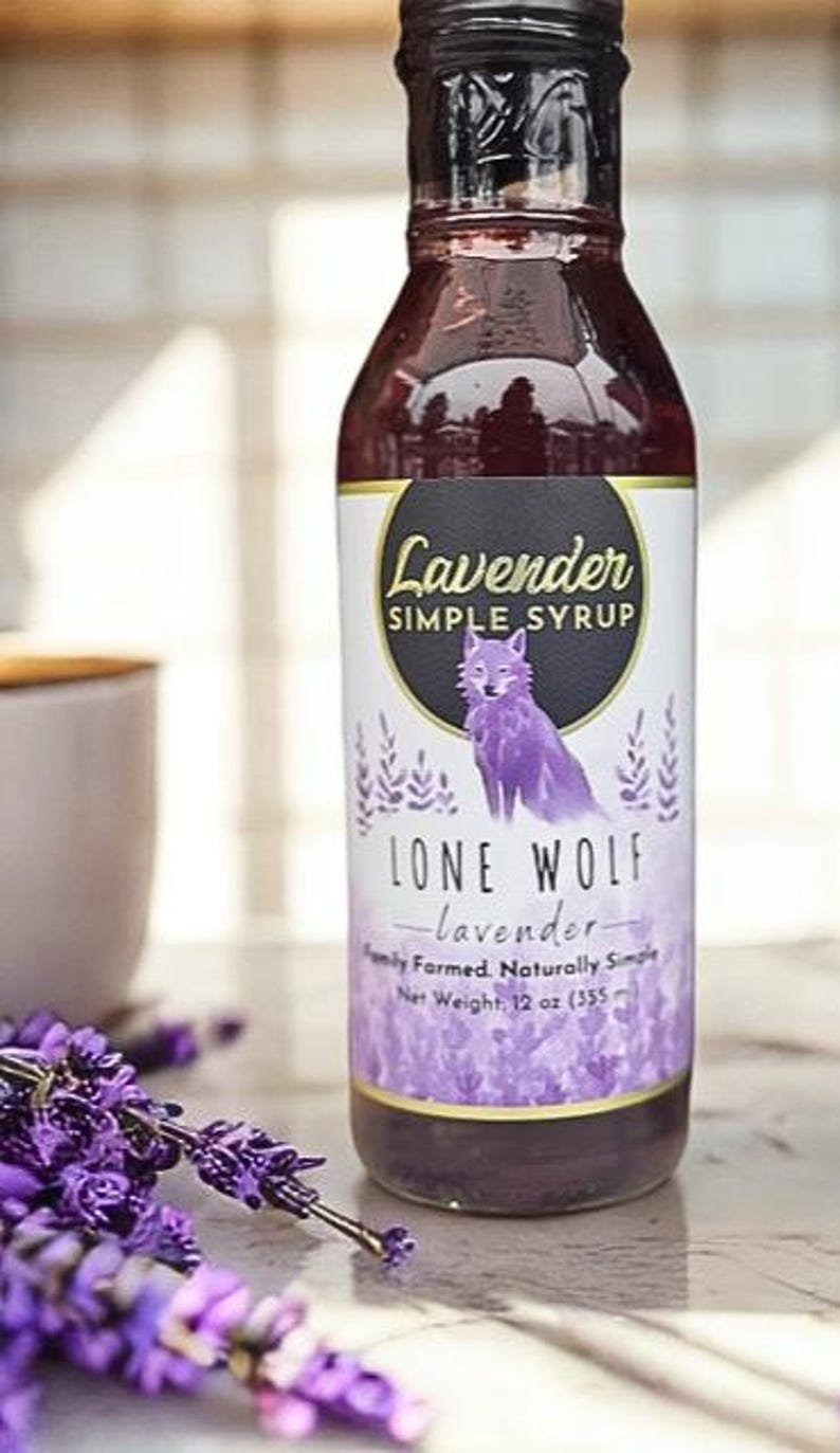 K&ouml;nnte beinhalten: Eine Glasflasche mit Lavendel-Sirup mit einer Illustration eines lila Wolfes auf dem Etikett. Das Etikett lautet "Lavender Simple Syrup" und "Lone Wolf - Lavendel - Familiengef&uuml;hrt. Nat&uuml;rlich einfach. Nettogewicht, 12 oz (355 ml)".