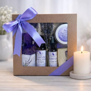May include: A brown cardboard gift box with a clear window, tied with a purple ribbon. Inside are lavender-scented products: hand and body lotion, pillow mist, body butter, a bar of soap, a sachet, and dried lavender stems, all labeled Lone Wolf.