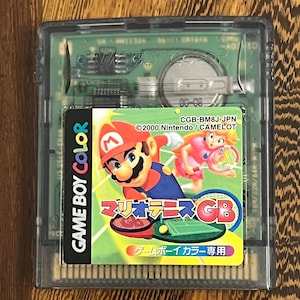 以下が含まれることがあります： マリオテニスGBのゲームボーイカラーカートリッジ。ラベルには、テニスをするマリオとピーチ姫が描かれています。カートリッジは透明なプラスチックケースに入っています。「GAME BOY COLOR」の文字が見えます。