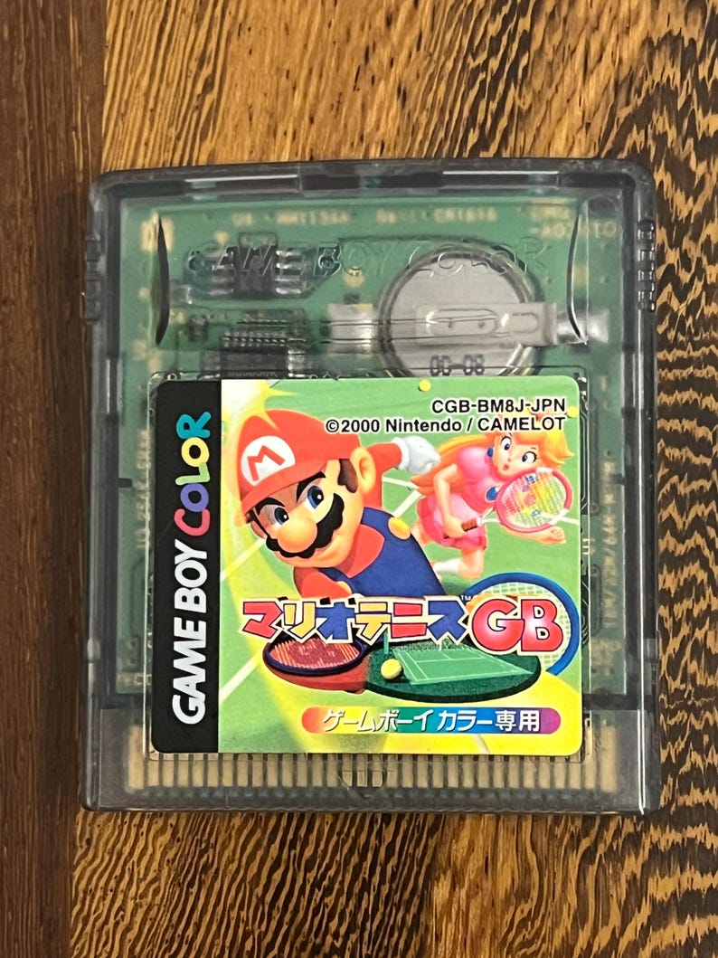 以下が含まれることがあります： マリオテニスGBのゲームボーイカラーカートリッジ。ラベルには、テニスをするマリオとピーチ姫が描かれています。カートリッジは透明なプラスチックケースに入っています。「GAME BOY COLOR」の文字が見えます。