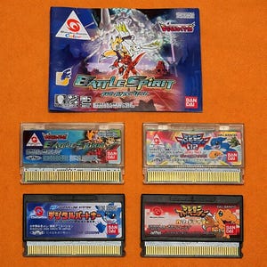 Puede incluir: Una colección de cartuchos de videojuegos Digimon y una caja de juego. La caja presenta ilustraciones coloridas con el texto "Battle Spirit". Los cartuchos muestran varios personajes de Digimon y texto japonés. El fondo es naranja liso.