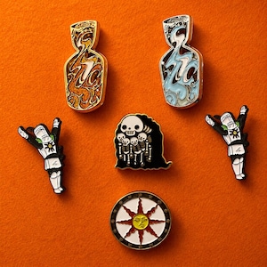 May include: An assortment of enamel pins on an orange background. The pins include two abstract figure designs, a skeleton with a black cloak, two knight figures, and a sun design with a face.