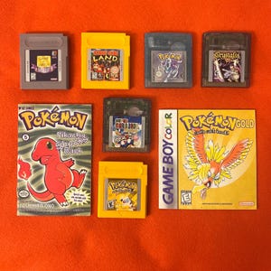 Op de afbeelding: Een verzameling Nintendo Game Boy-videogamecartridges waaronder Game & Watch Gallery, Donkey Kong Land, Pokemon Crystal, Crystalis, Super Mario Bros. Deluxe en Pokemon Yellow, samen met een Pokemon-stripboek en een Pokemon Gold-handleiding.