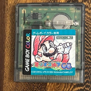 以下が含まれることがあります： マリオゴルフのゲームボーイカラーカートリッジ。ラベルには、赤い帽子とオーバーオールを着てゴルフのクラブを持っているマリオが描かれています。「GAME BOY COLOR」と日本語のテキストが含まれています。カートリッジは透明なプラスチックケースに入っています。