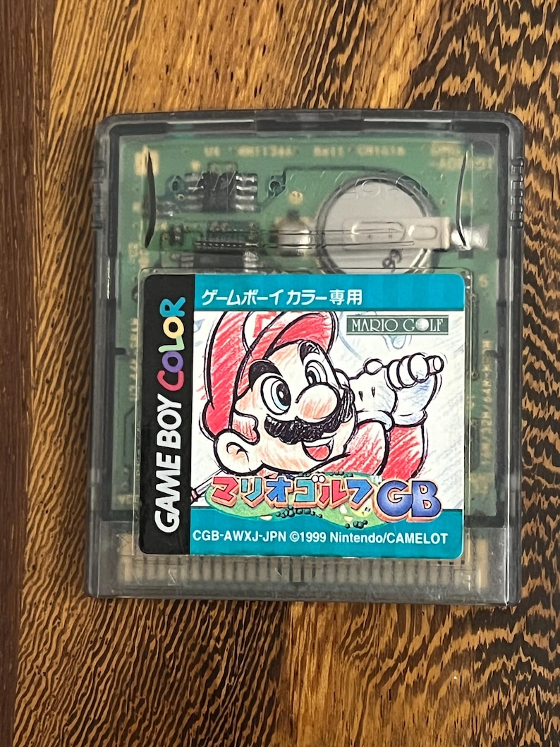 以下が含まれることがあります： マリオゴルフのゲームボーイカラーカートリッジ。ラベルには、赤い帽子とオーバーオールを着てゴルフのクラブを持っているマリオが描かれています。「GAME BOY COLOR」と日本語のテキストが含まれています。カートリッジは透明なプラスチックケースに入っています。