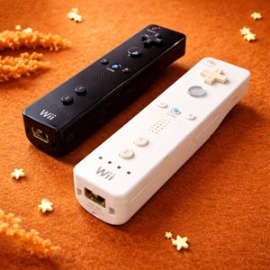 Puede incluir: Dos mandos de Wii, uno negro y otro blanco, se muestran sobre una superficie naranja. El mando negro tiene botones negros, mientras que el mando blanco tiene botones blancos. Ambos mandos tienen el logotipo de Wii y un puerto en la parte inferior.