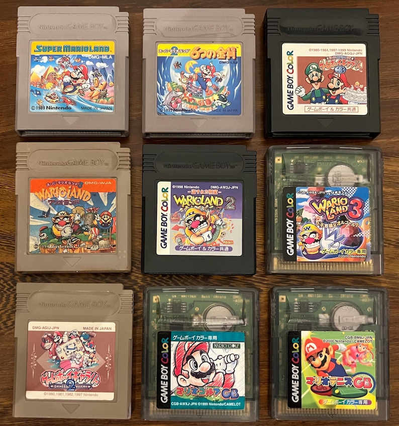以下が含まれることがあります： カラフルなゲームラベルが付いた9つのニンテンドーゲームボーイカートリッジが表示されています。「スーパーマリオランド」、「ワリオランド」、「マリオゴルフGB」などのタイトルが含まれています。カートリッジの色は、グレー、ブラック、クリアなど様々です。