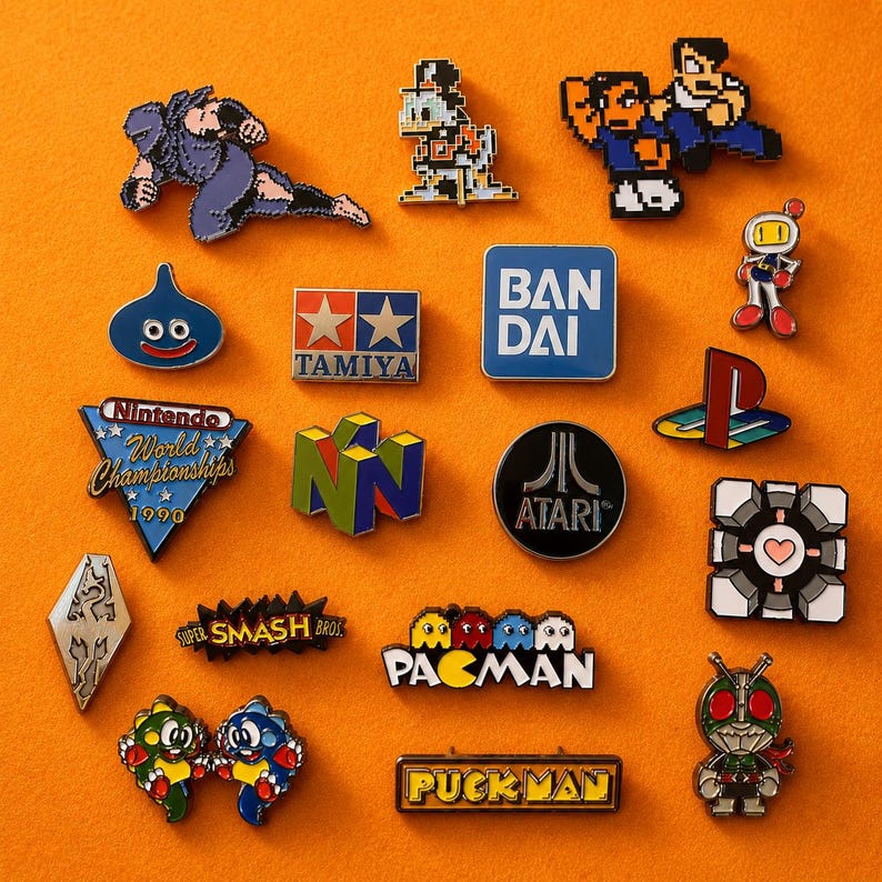 May include: A collection of colorful enamel pins featuring video game and pop culture themes. Designs include characters from Pac-Man, Nintendo, and Atari, along with logos and other iconic imagery. The pins are arranged on an orange surface.