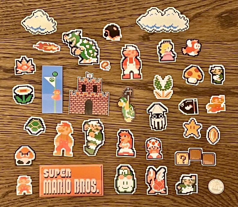 Może przedstawiać: Kolekcja pikselowych naklejek Super Mario Bros. z postaciami takimi jak Mario, Peach i Bowser, a także kultowymi elementami, takimi jak chmury, grzyby i bloki ze znakiem zapytania. Naklejki ułożone są na drewnianej powierzchni, z prostokątną naklejką z napisem "Super Mario Bros."